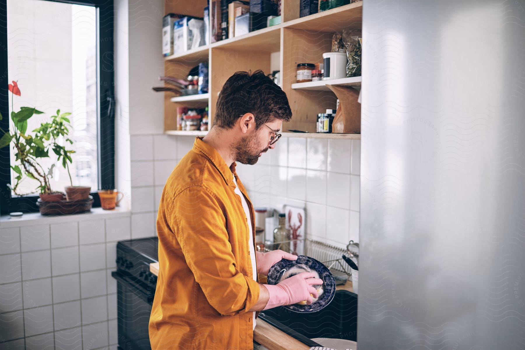 a man wearing glasses in the kitchen sink doing the dishes