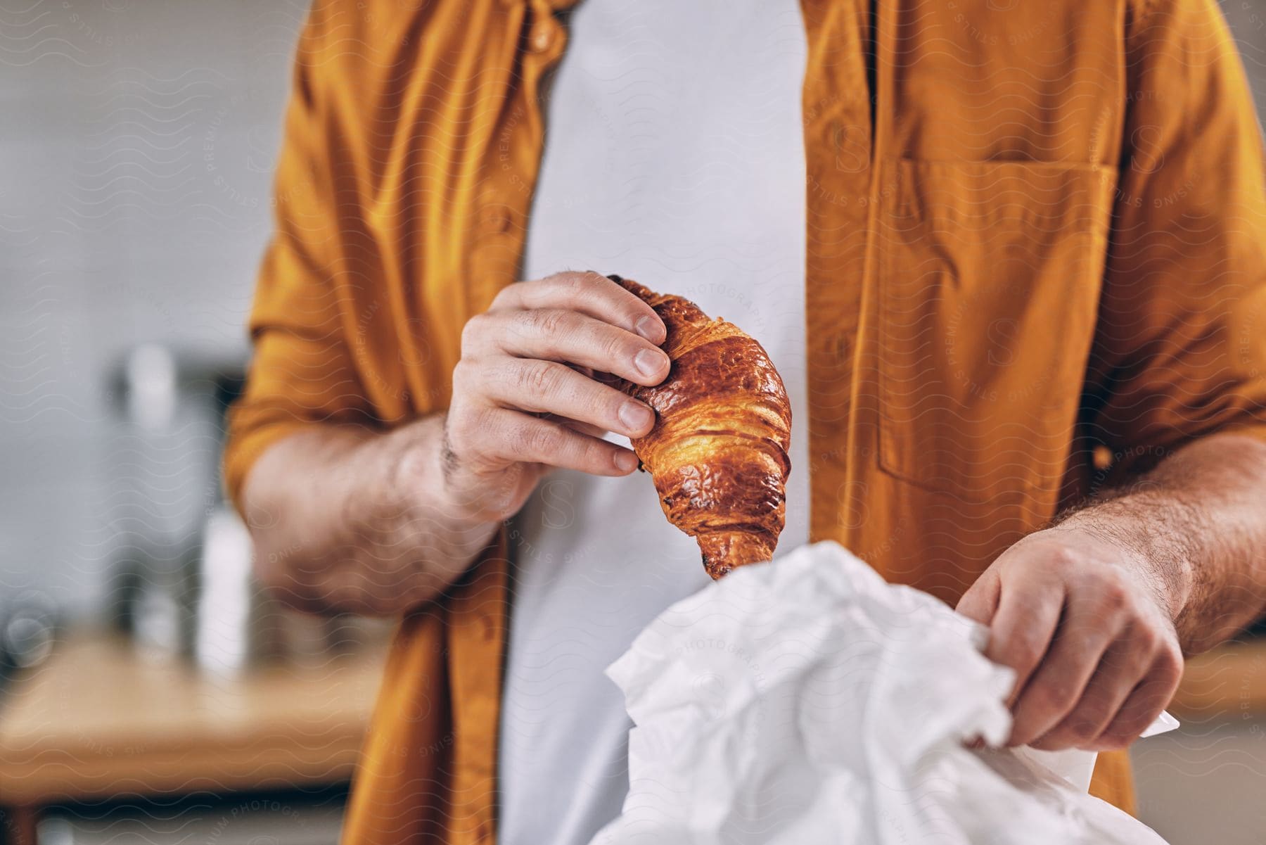 A man taking out a croissant from a plastic  bag.