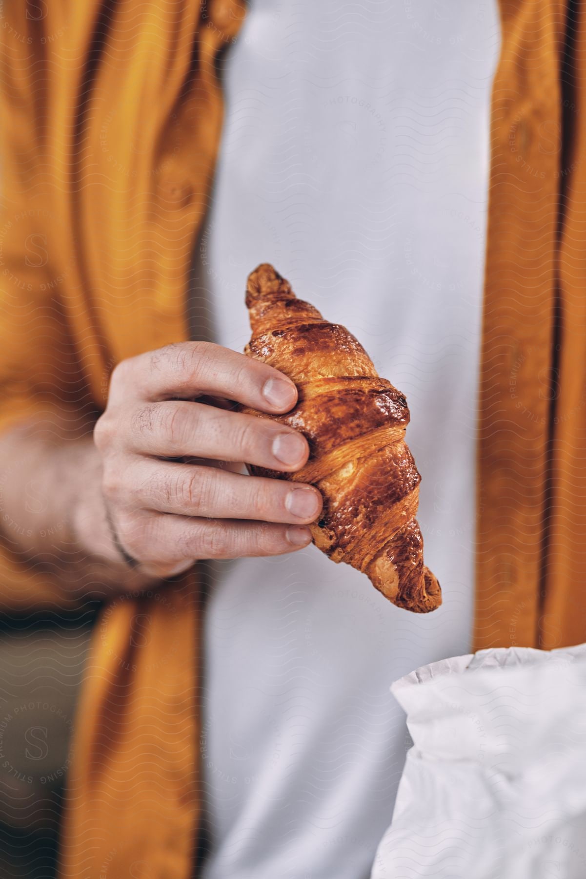 Man holds croissant  near open pastry bag.