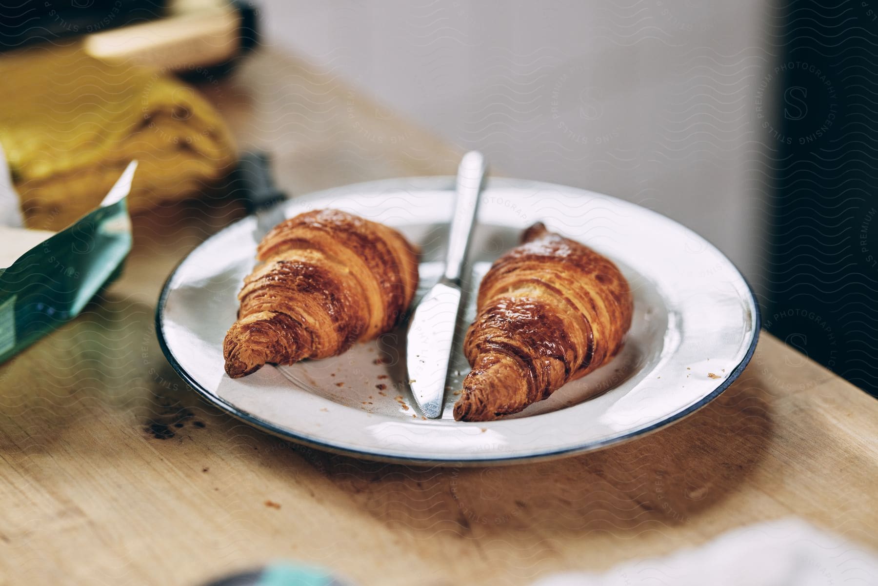 Two baked croissants sit on a white plate with a knife between them.