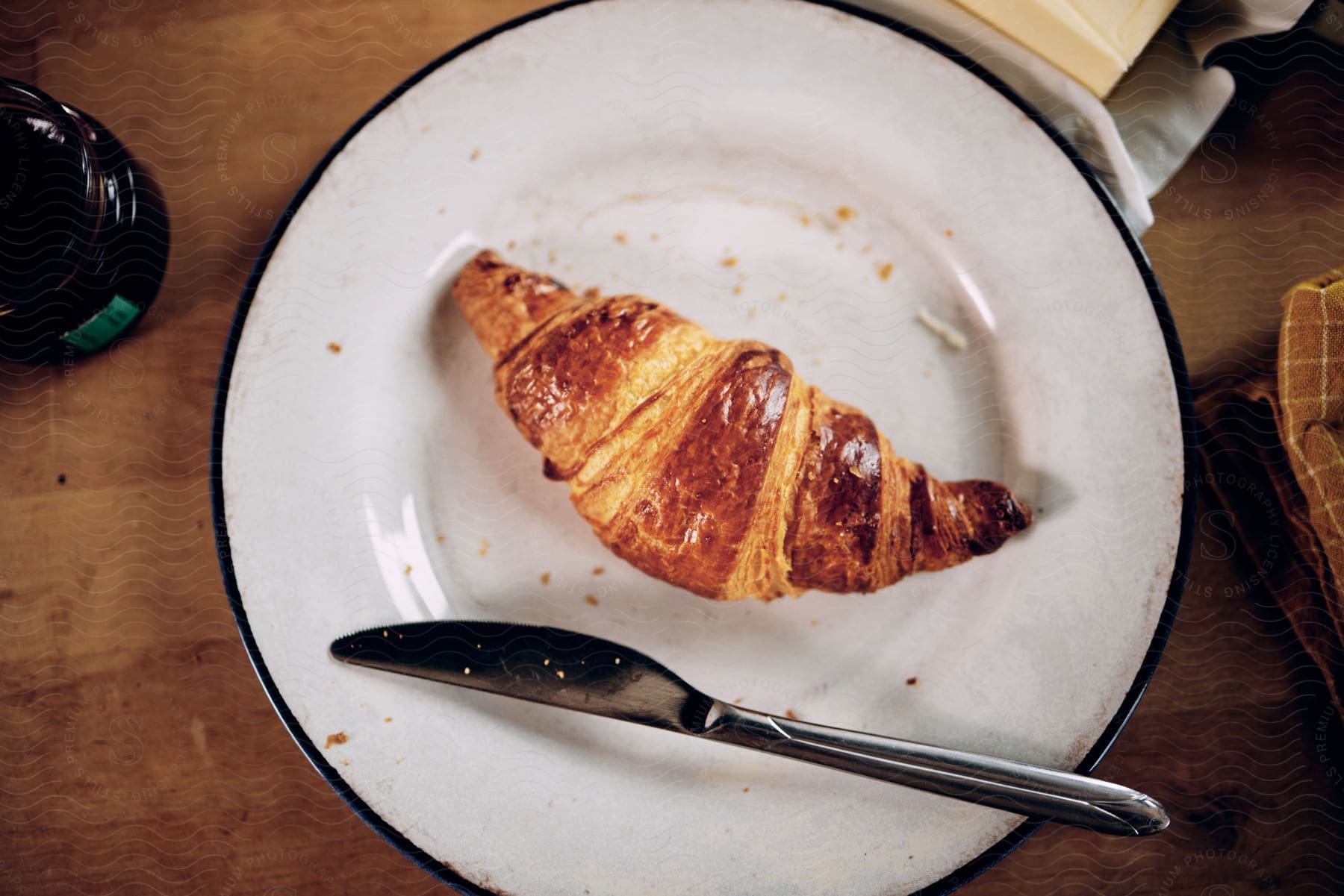 a white plate on a table with a butter knife and a croissant on it