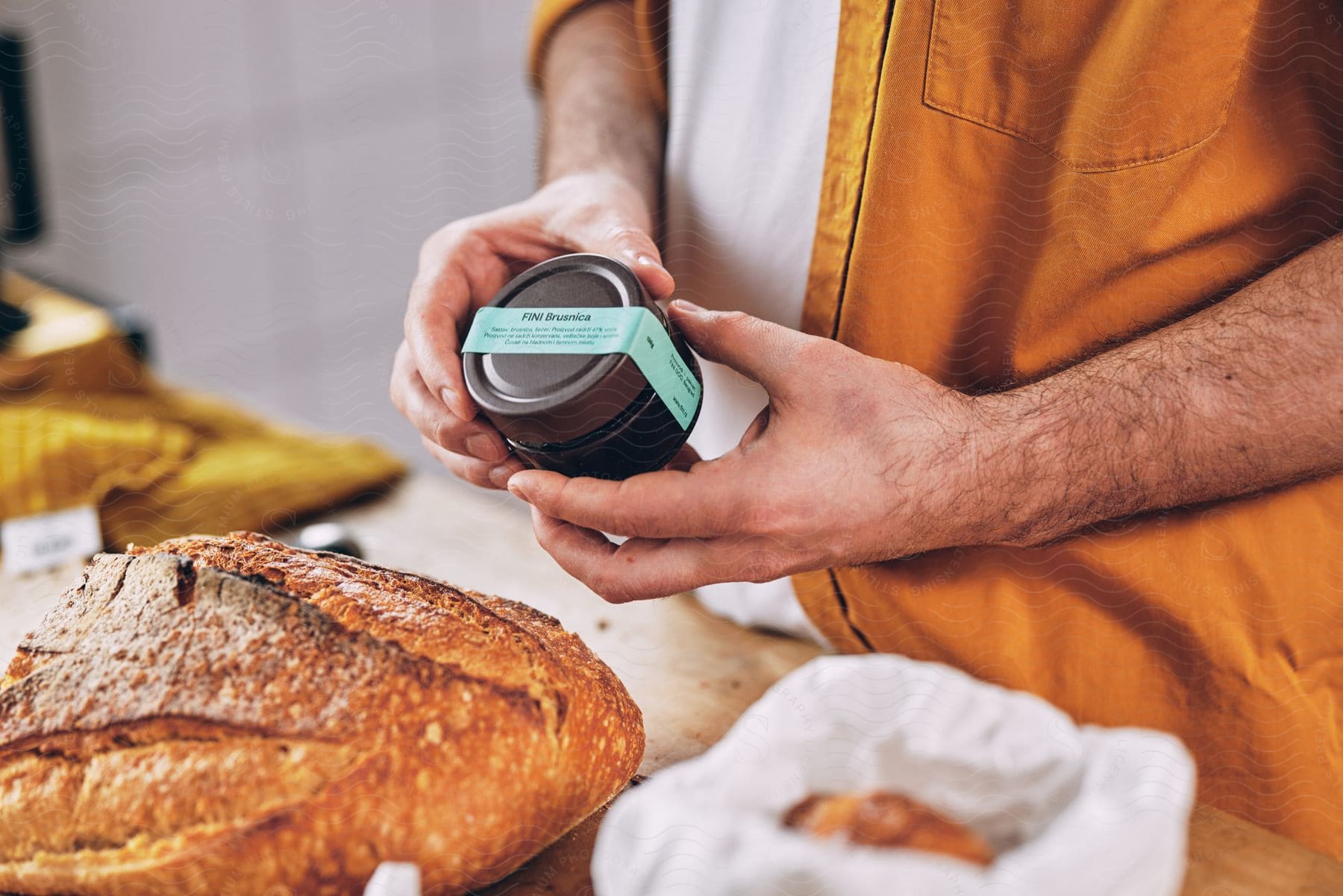 A man holds an unopened jar of spread above a loaf of crusty bread.