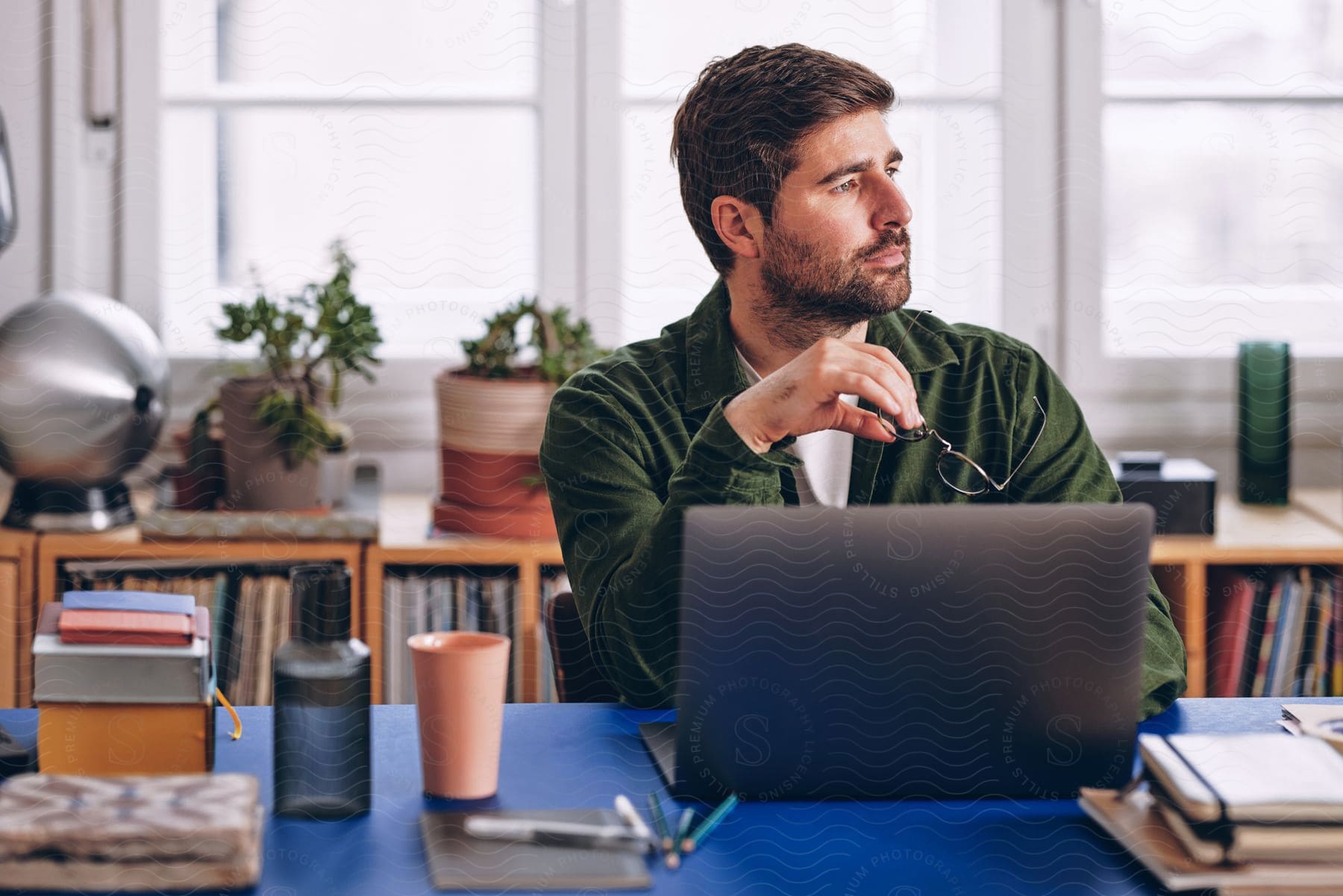 Bearded man wearing a green shirt sits at a desk looks away while using a laptop