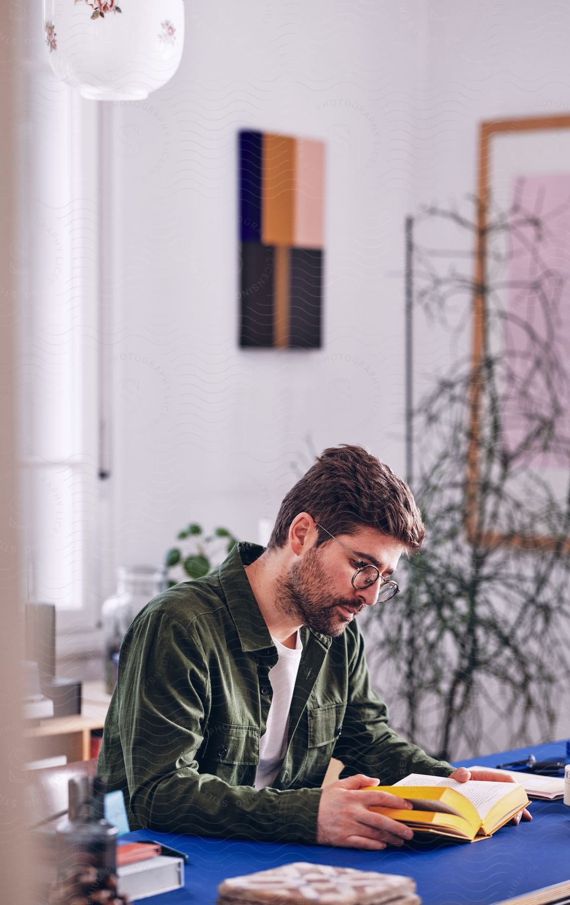 Bearded man with glasses and a green shirt sits at desk reading a book