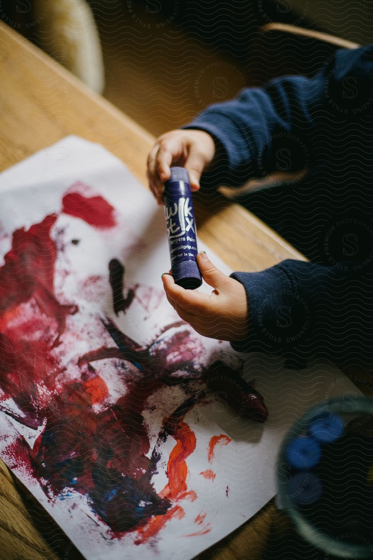 Hands hold tempera paint tube over red stained canvas