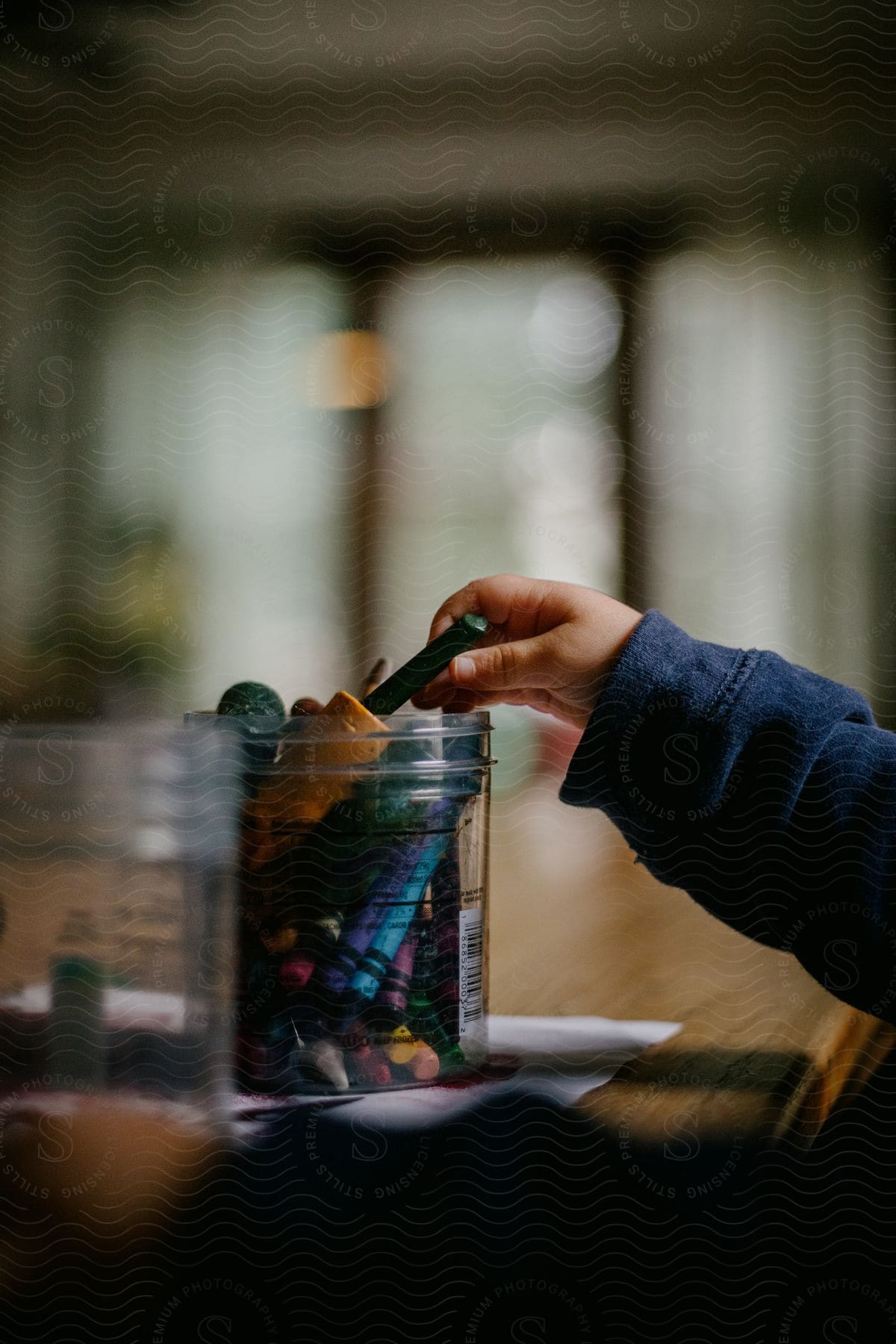 A child reaches for a crayon from a jar of crayons on top of a sheet of paper