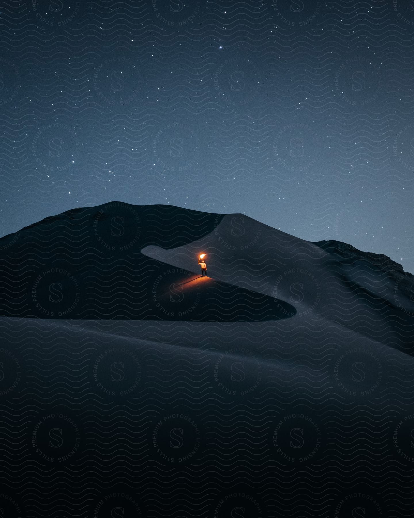 Stock photo of a man standing on a sand dune at night while holding up a flame.