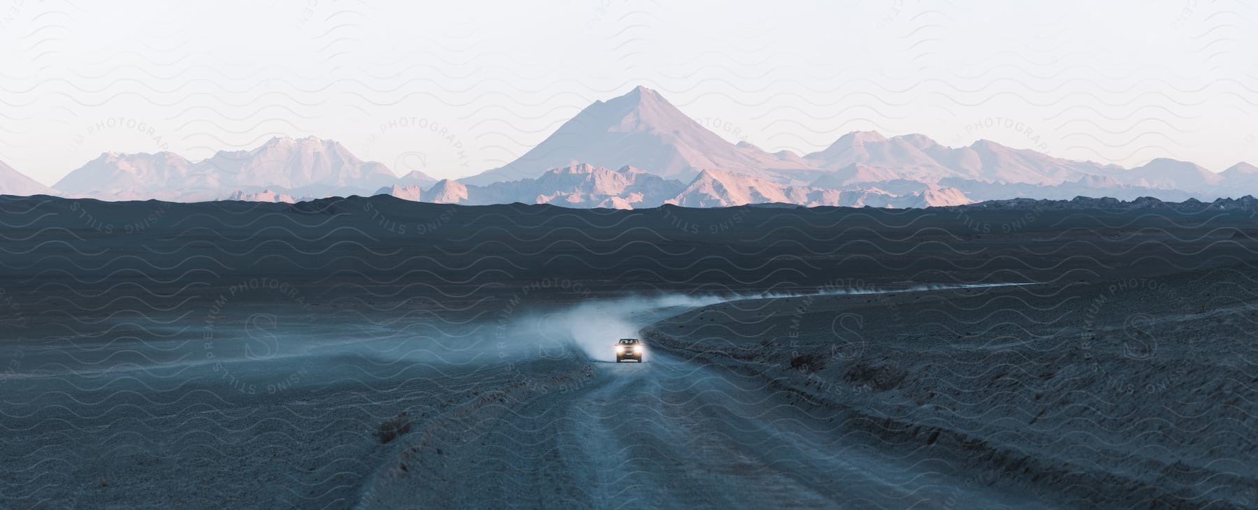 A dune buggy travels through the desert leaving a trail of smoke behind and mountains in the distance