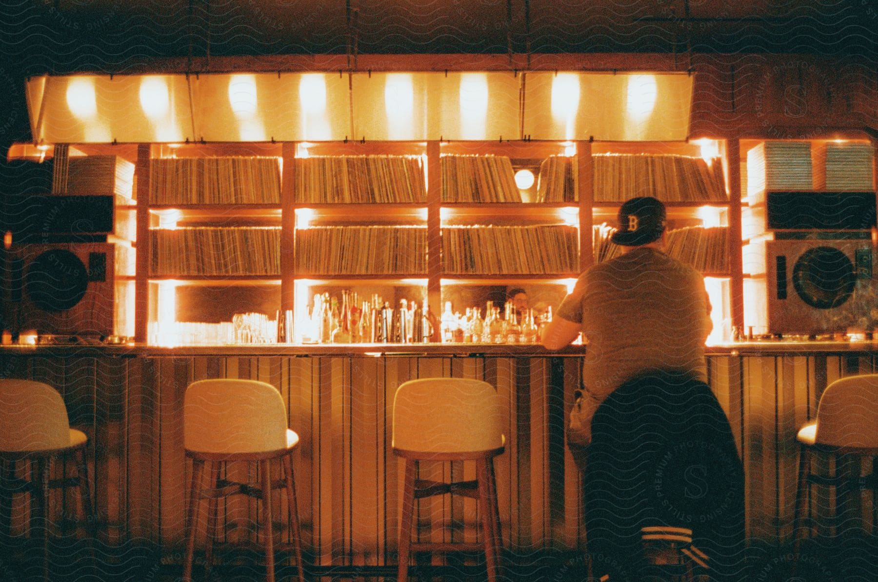 Man sitting in a chair facing a bar counter with drinks.