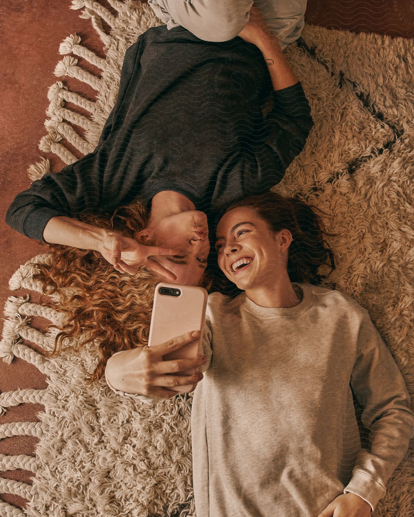 Women lying on a rug, laughing and taking a selfie