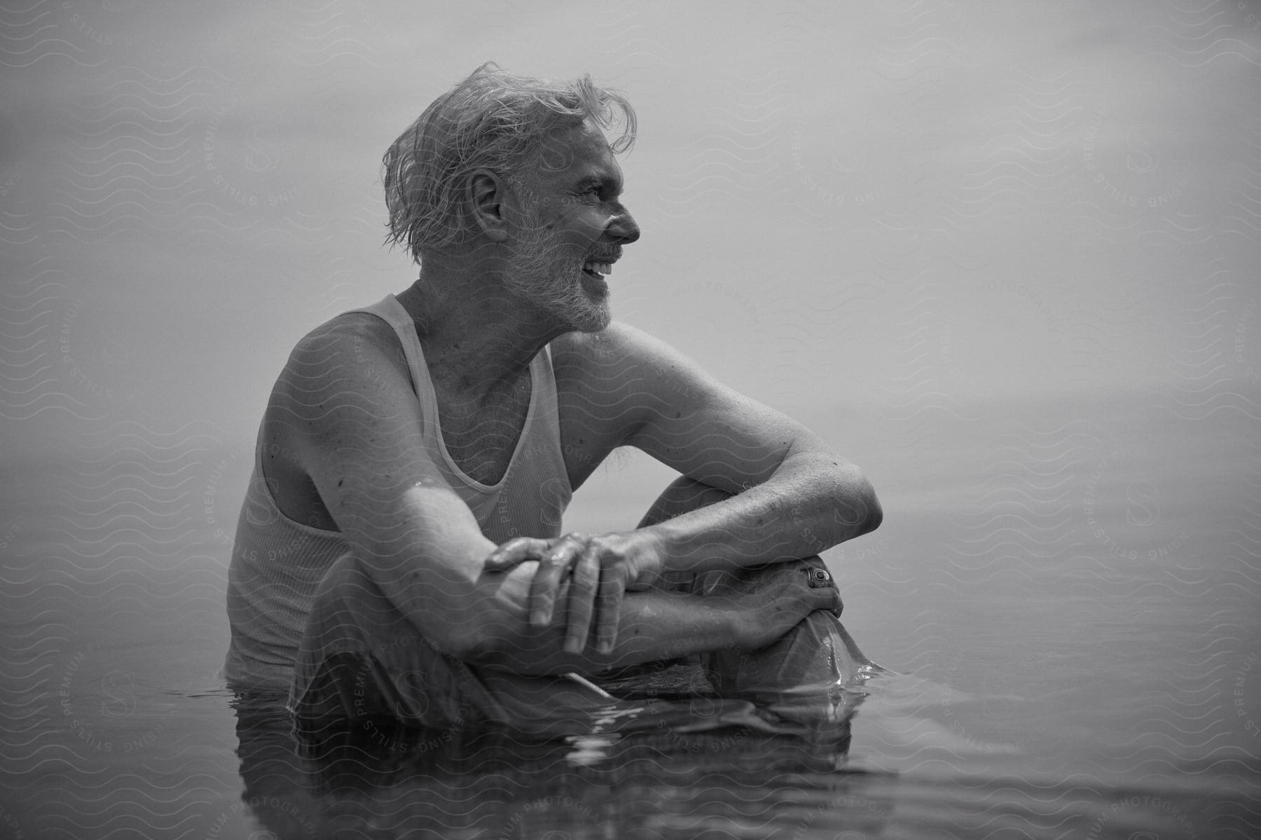 Older man in a sleeveless top smiling and resting in calm water.