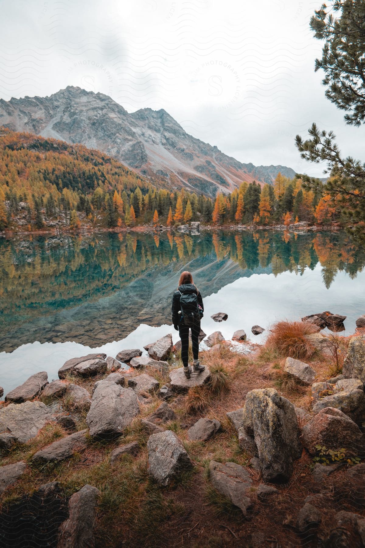 A woman at the lakeside looking at the mountains on the horizon.