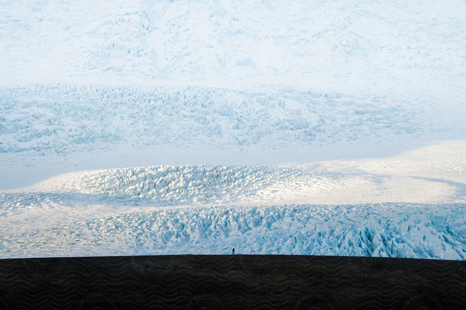 A person walks along a plateau overlooking a massive ice field.