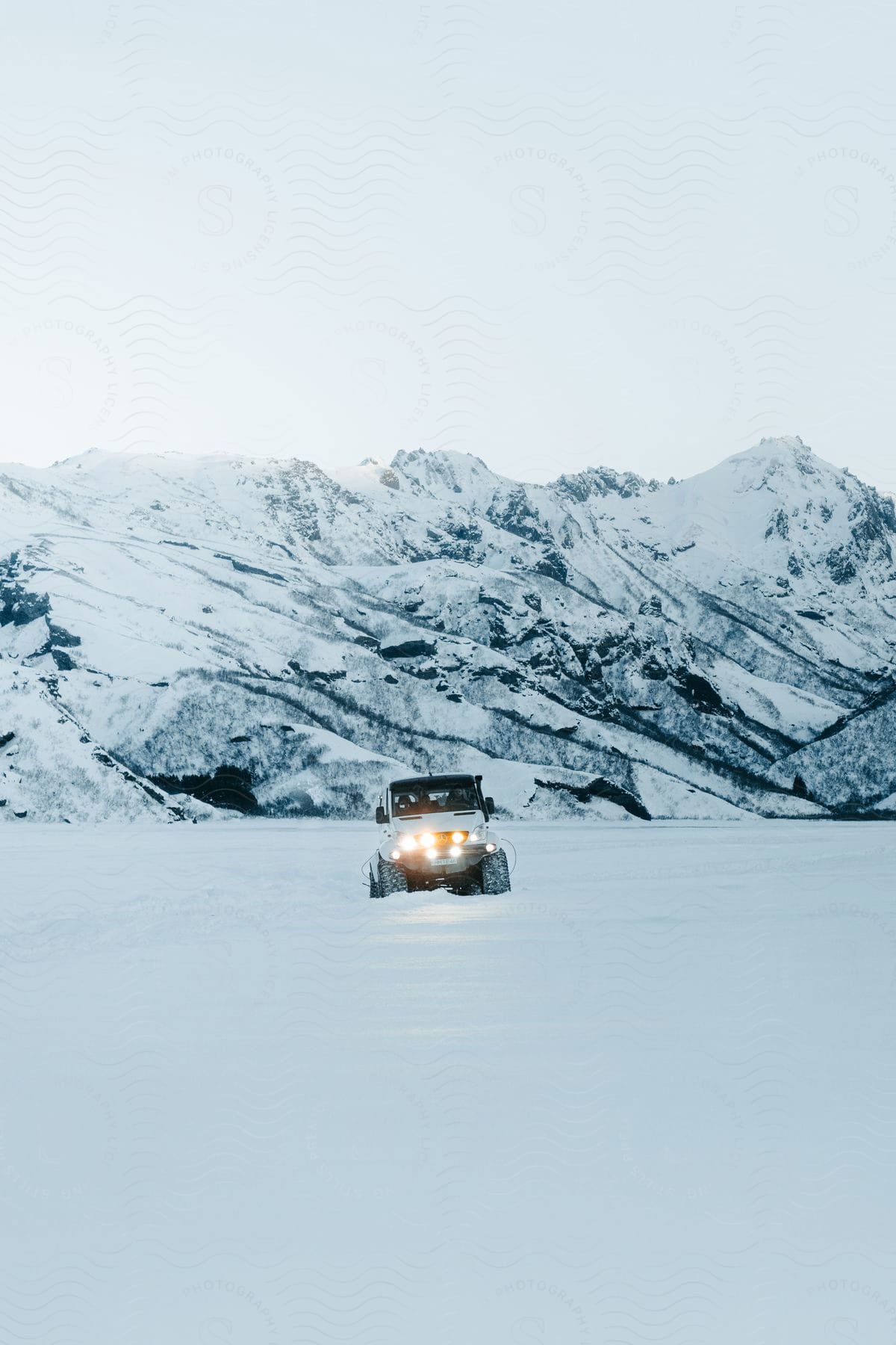 A truck with headlights on is traveling across the arctic snow with glacial landforms in the distance