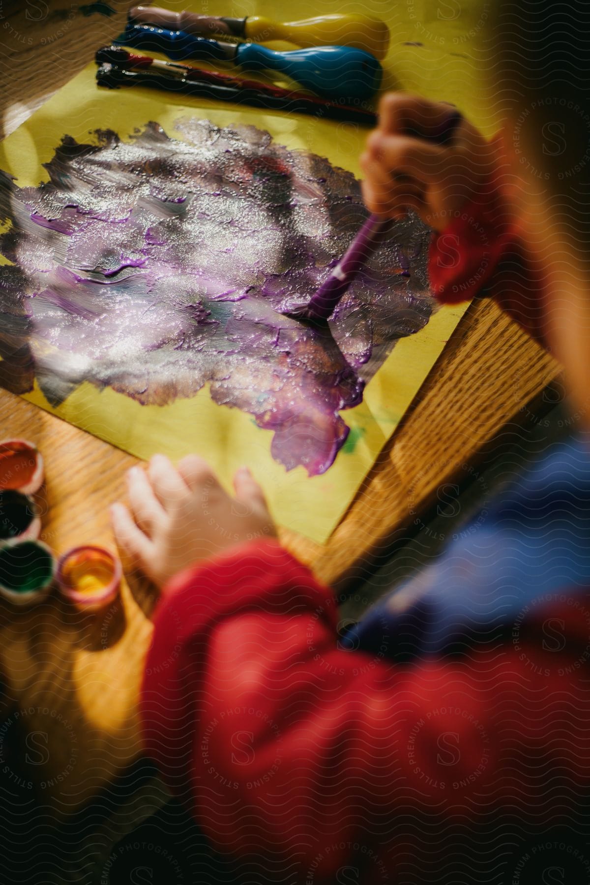 A child is holding a paint brush in one hand and holding the paper with the other hand as they paint a picture