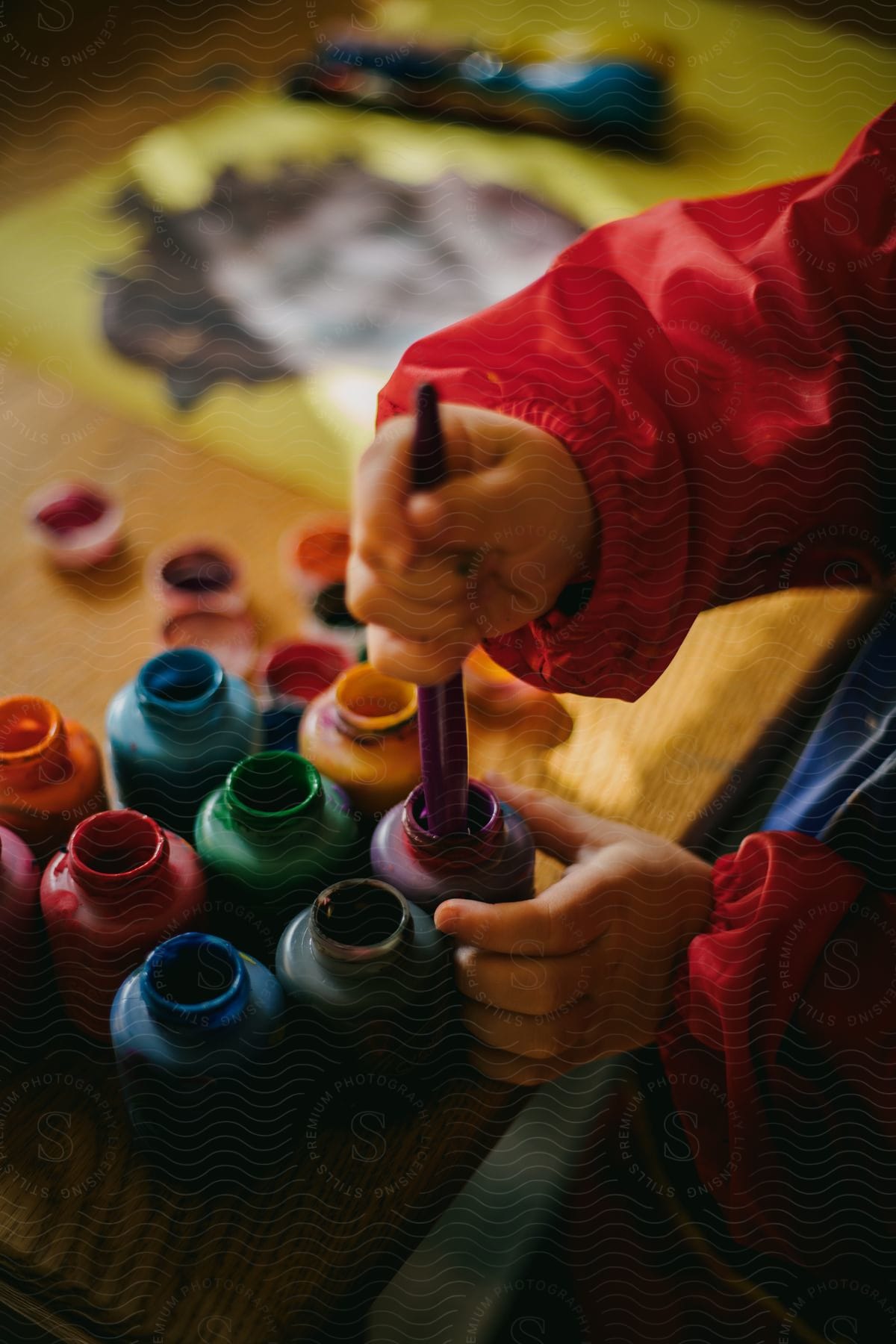 a child holding a paint brush in a bottle of paint.