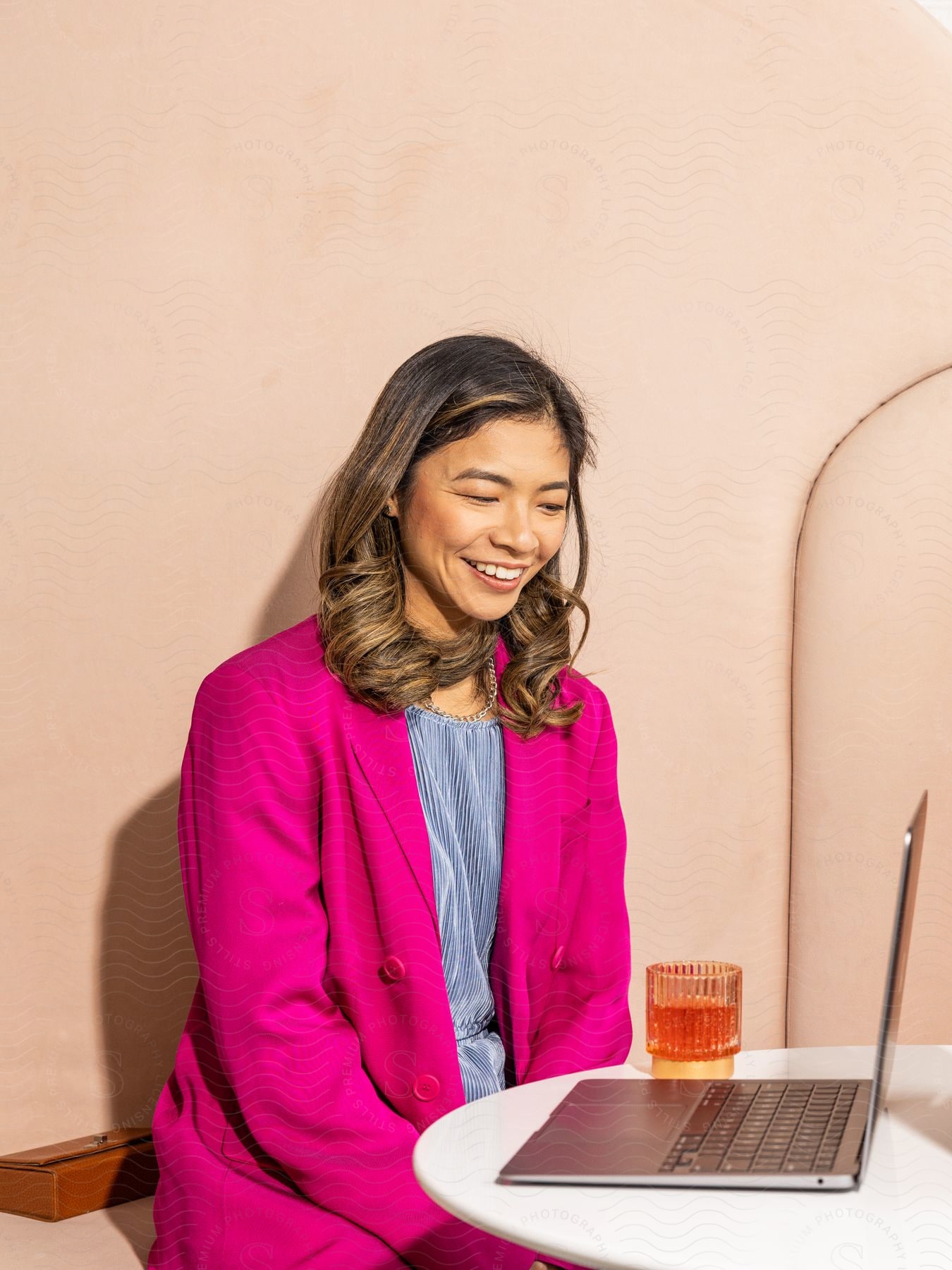 Stock photo of a woman is sitting at a table with a laptop computer as she smiles and laughs