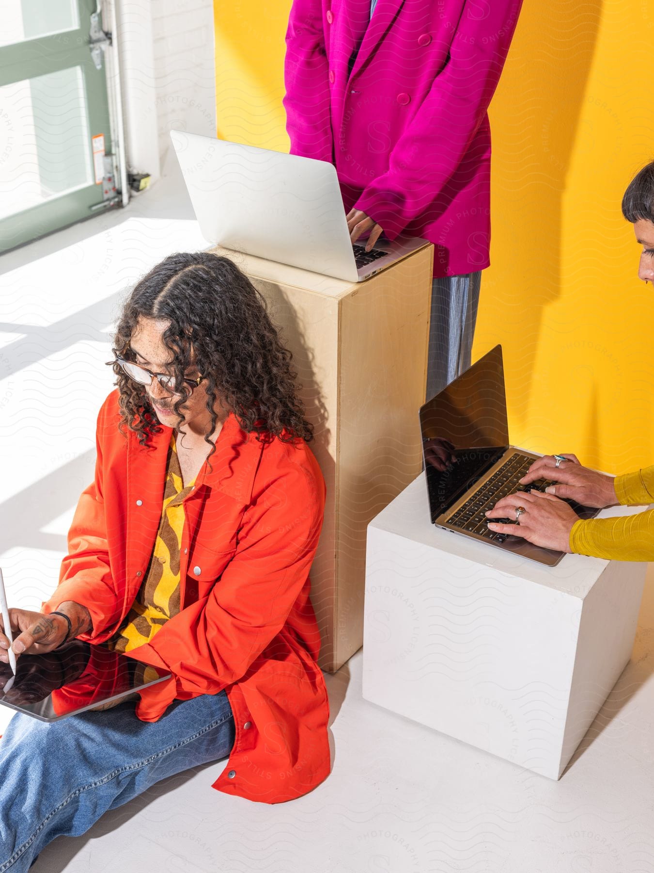 Three brightly clothed people using laptops and a tablet.