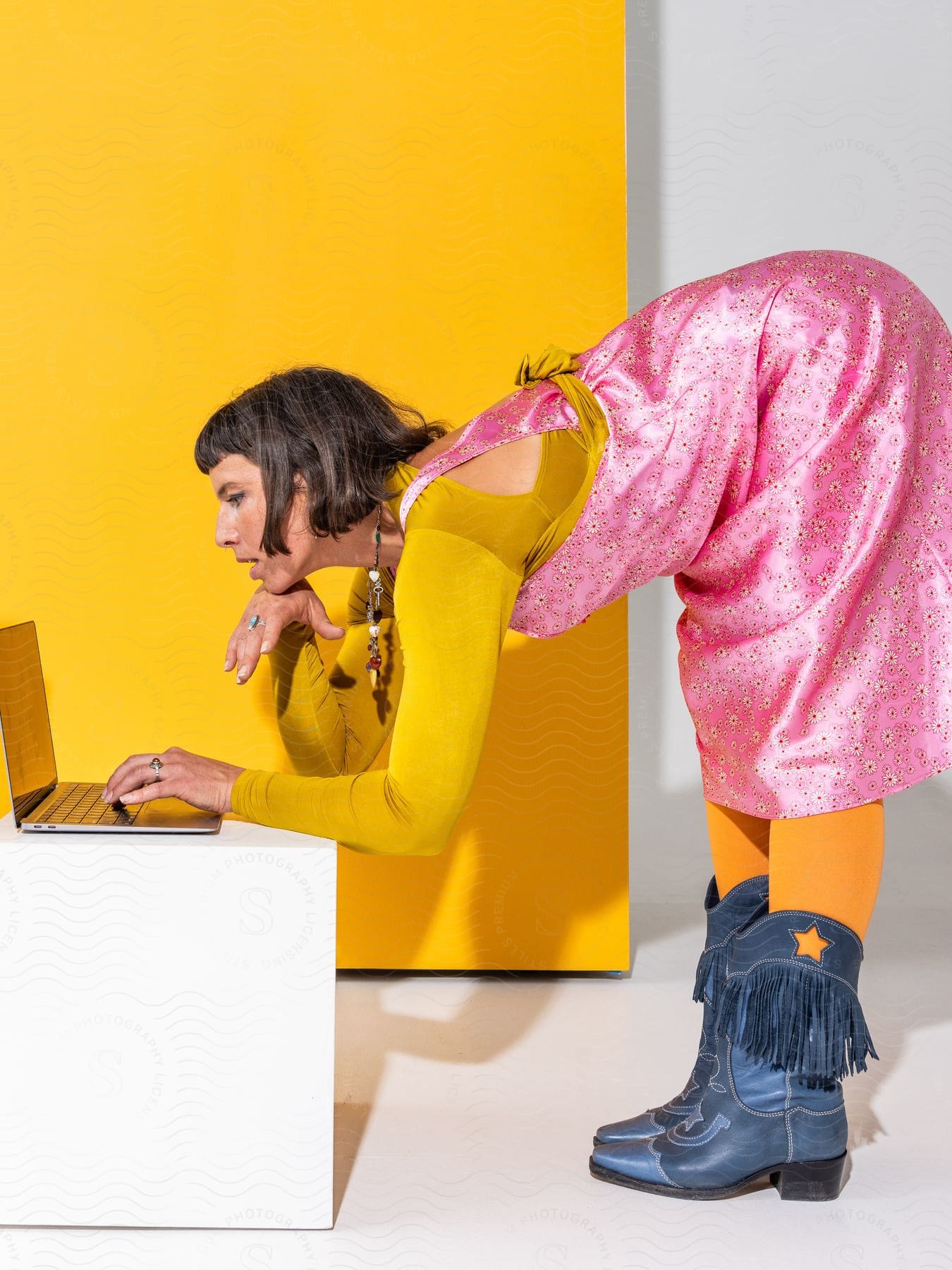 Stock photo of a brightly clothed woman bending over to type on a laptop.