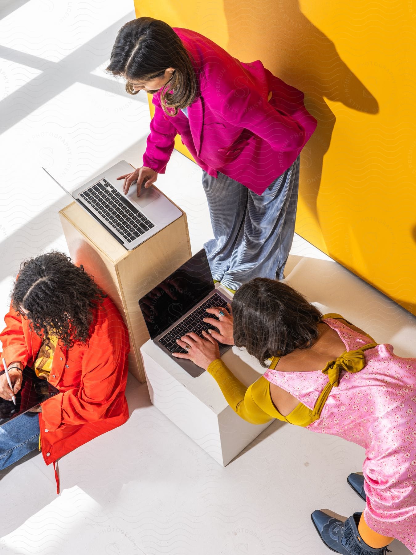 three young lady in different posture as two of them are working on their laptop while the other is seated and is working on her tablet