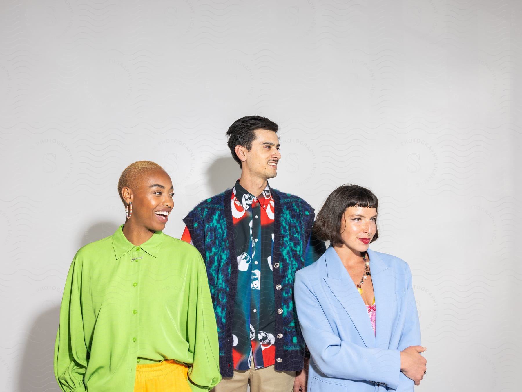 Two women and one man posing and modeling in fashionable clothing with expressions of happiness.