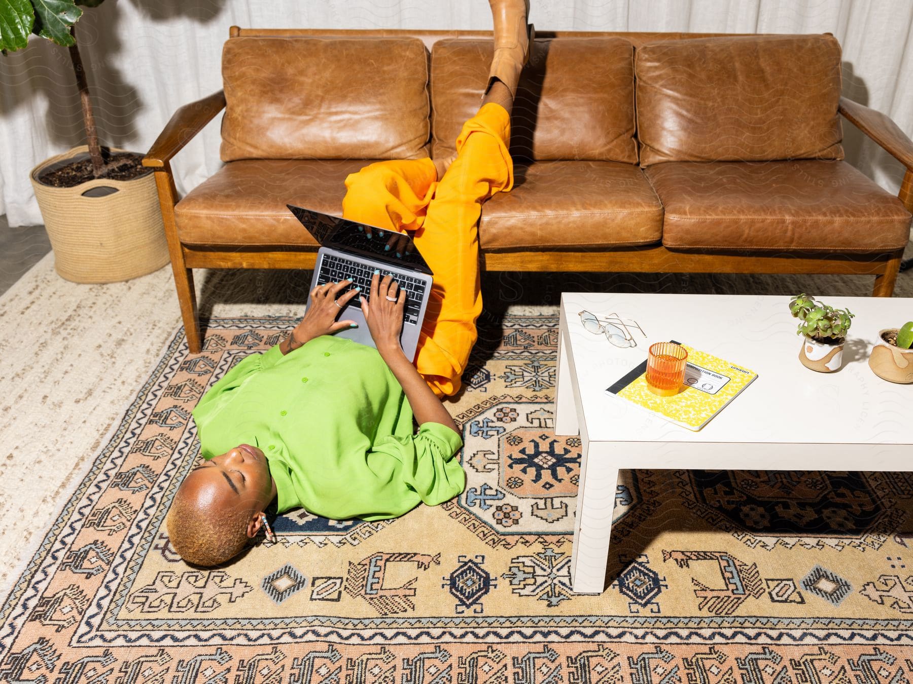 A woman is lying on the floor with her feet on the couch as she types on a laptop computer