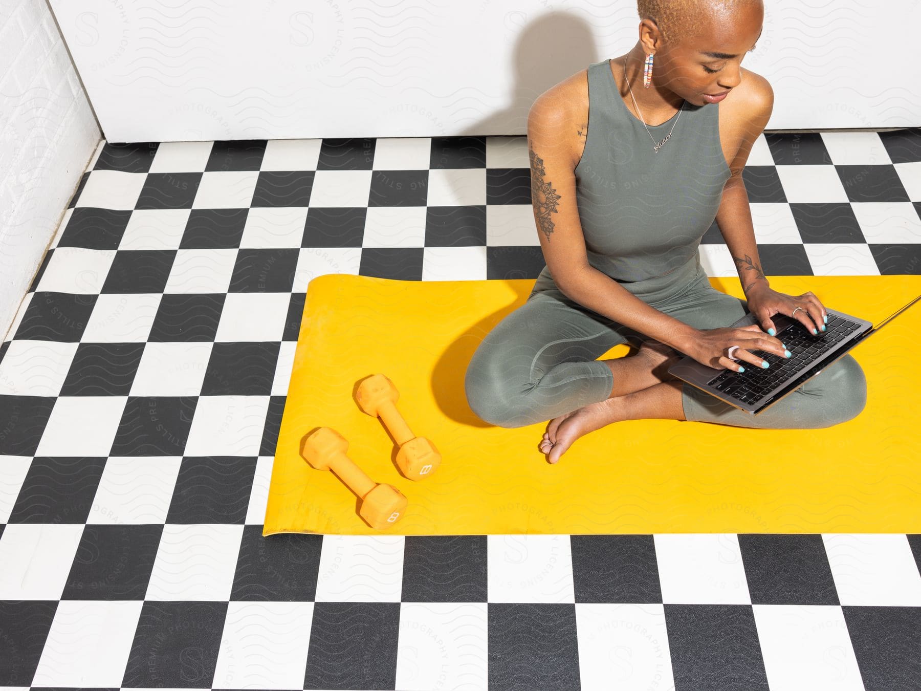 Stock photo of a women is sitting on her exercising mat as she types on her lap top.