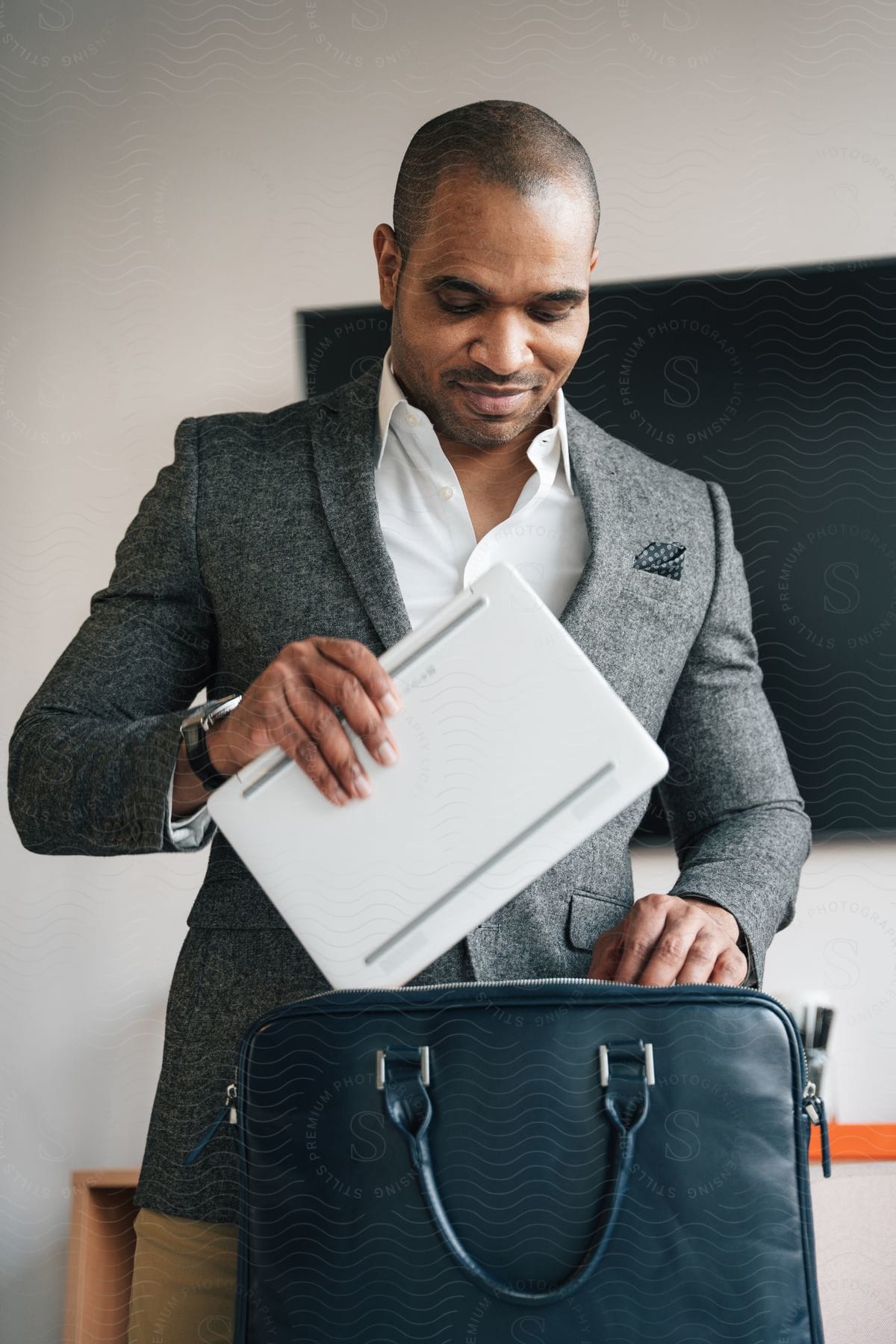 Stock photo of man smiles while standing in office and putting laptop into briefcase.