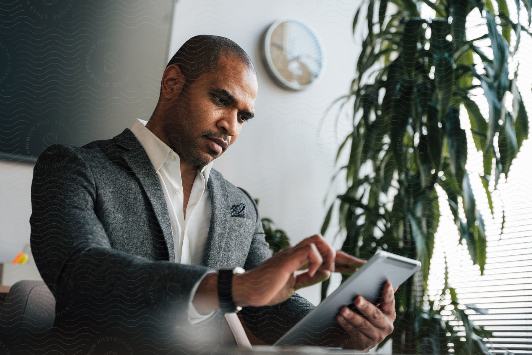 A man in a grey suit watches his tablet while at the office.