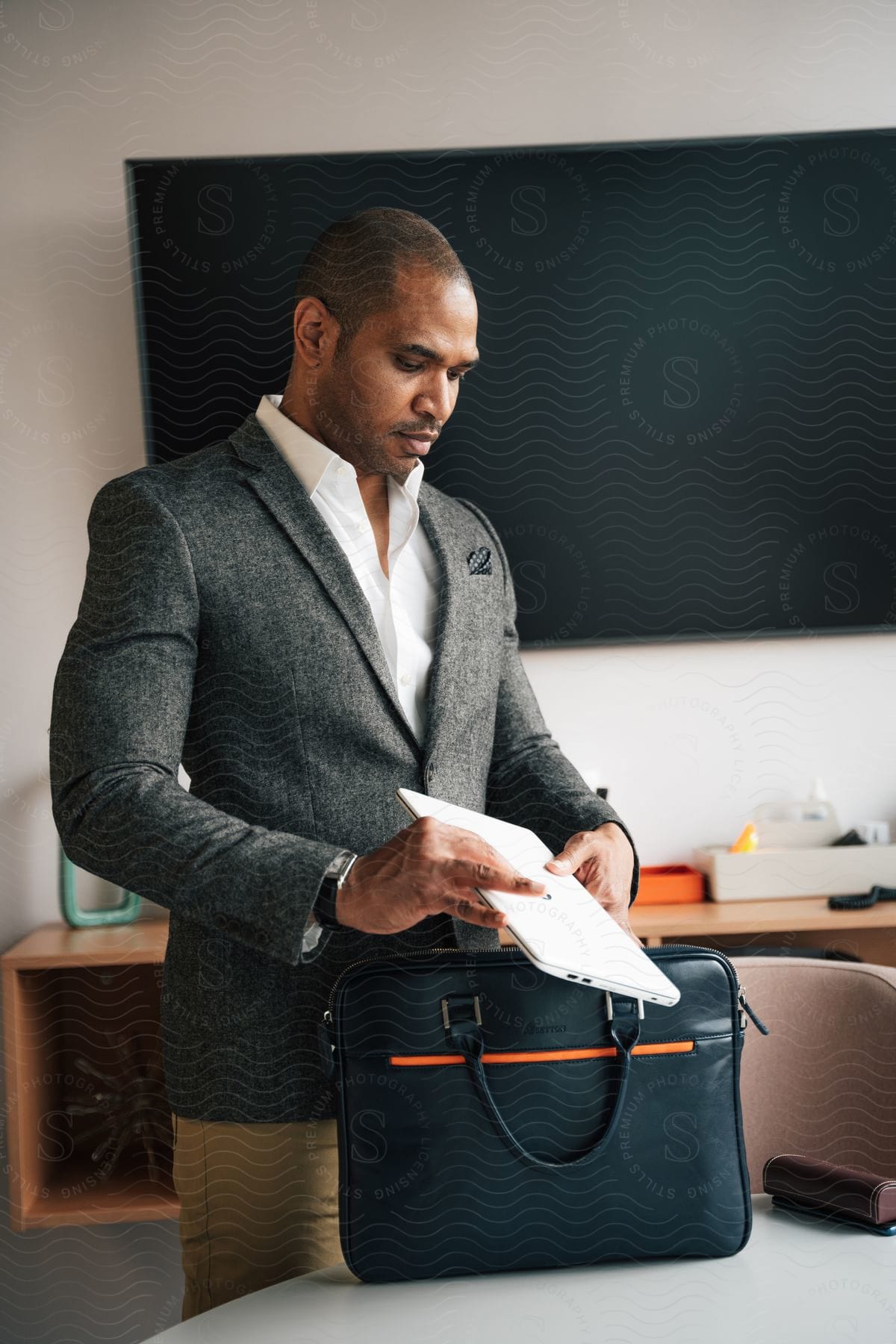 A man in a blazer stands while placing his laptop computer into a bag to carry it.