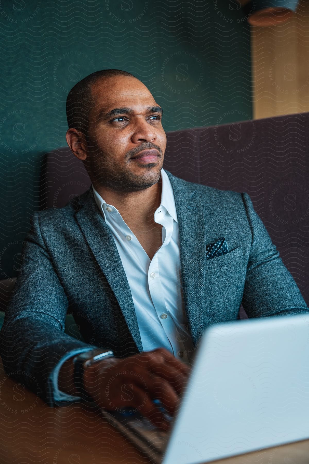 Man in a suit sitting, looking forward, with his laptop under the table.