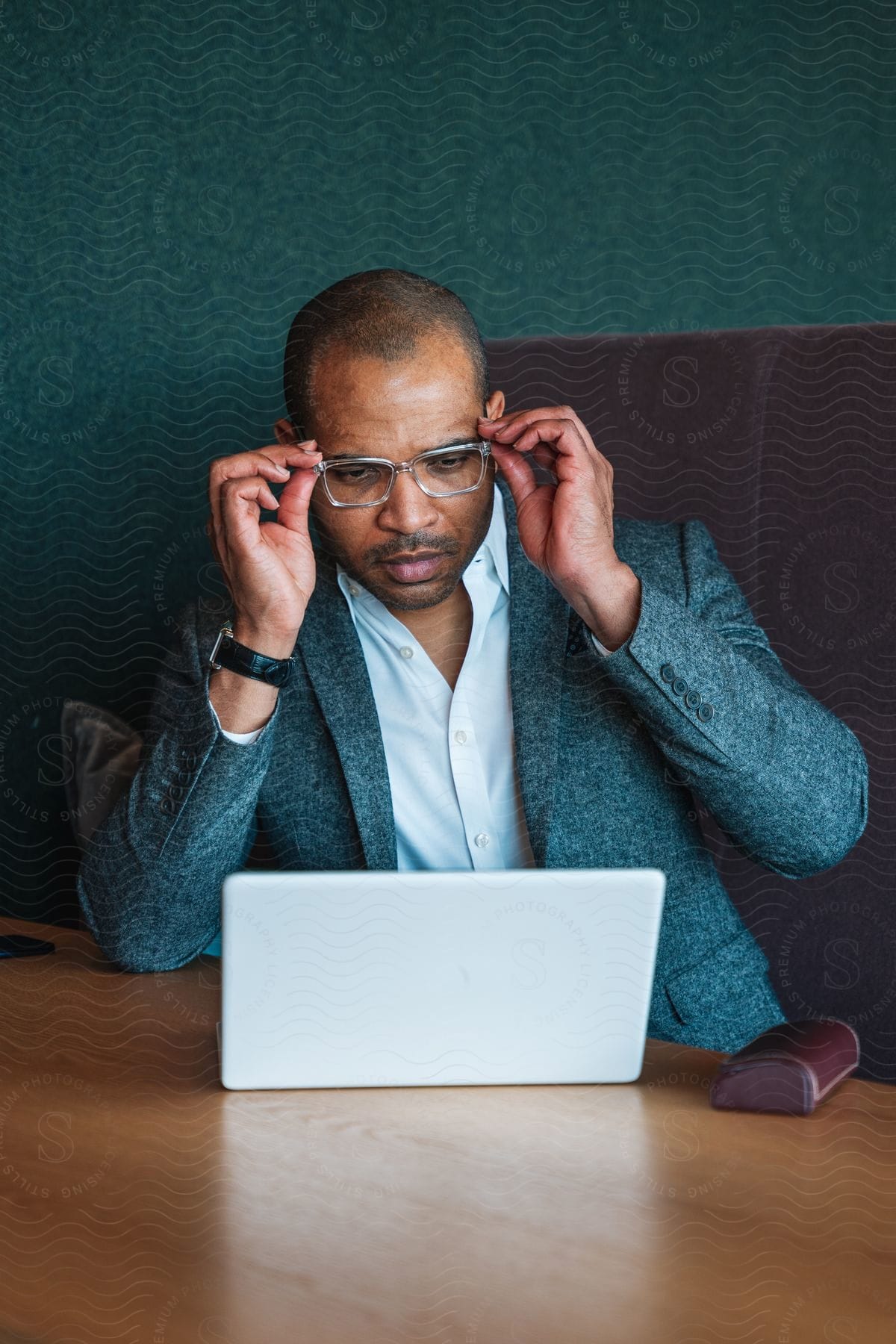 Stock photo of a man is positioning his glasses on his face as he looks at his laptop at his work desk.