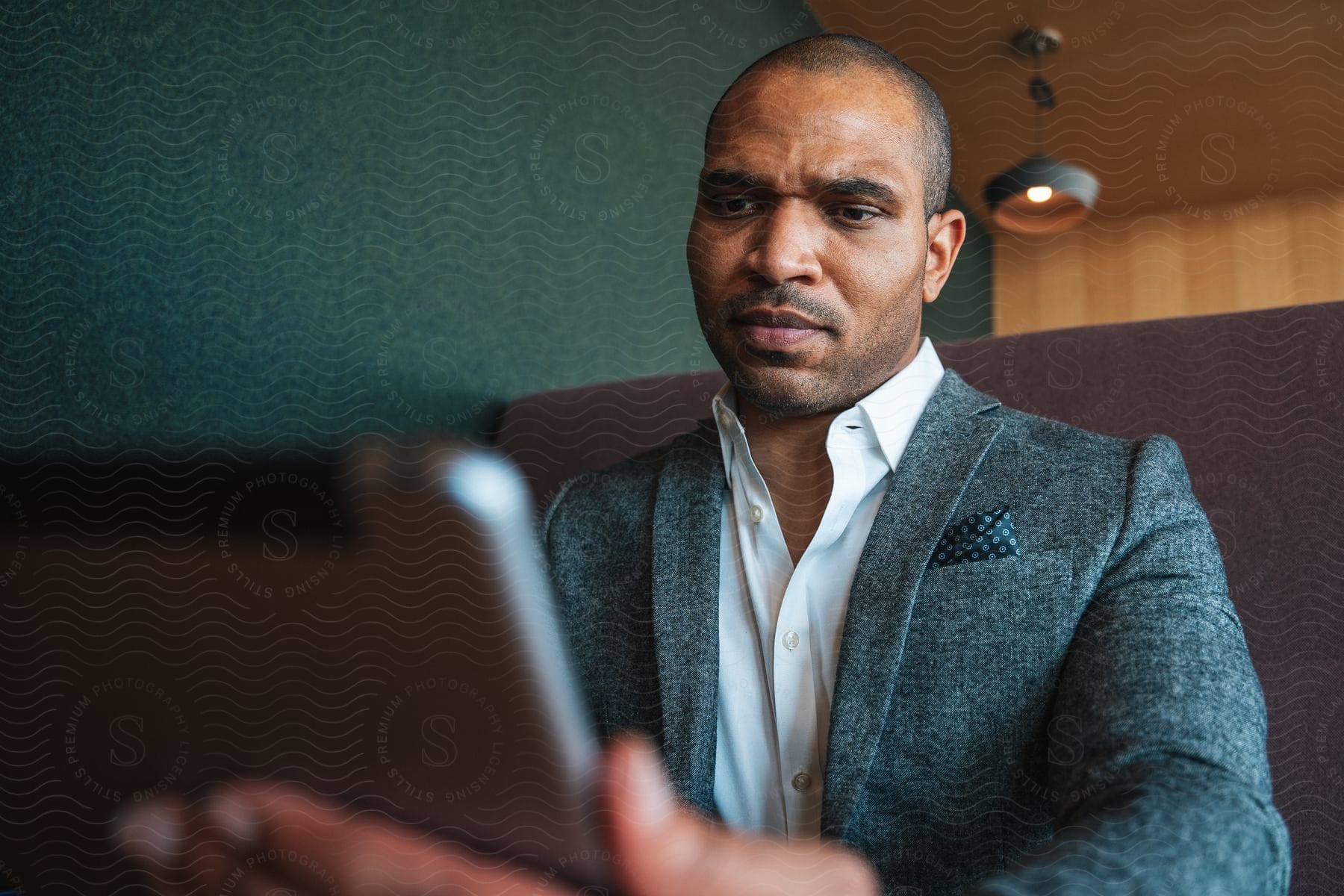 A businessman wearing a suit is watching his tablet while sitting on a brown sofa.