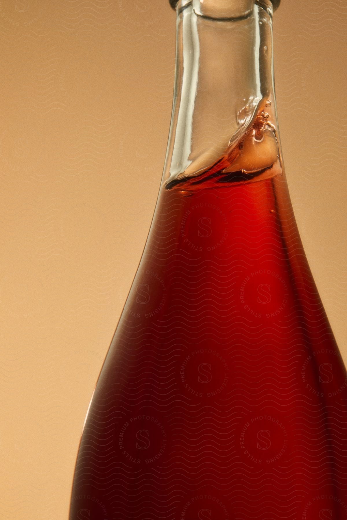 A smooth glass bottle containing an amber liquid that is tilted up against one side of the bottle shown against a flat, pale orange background