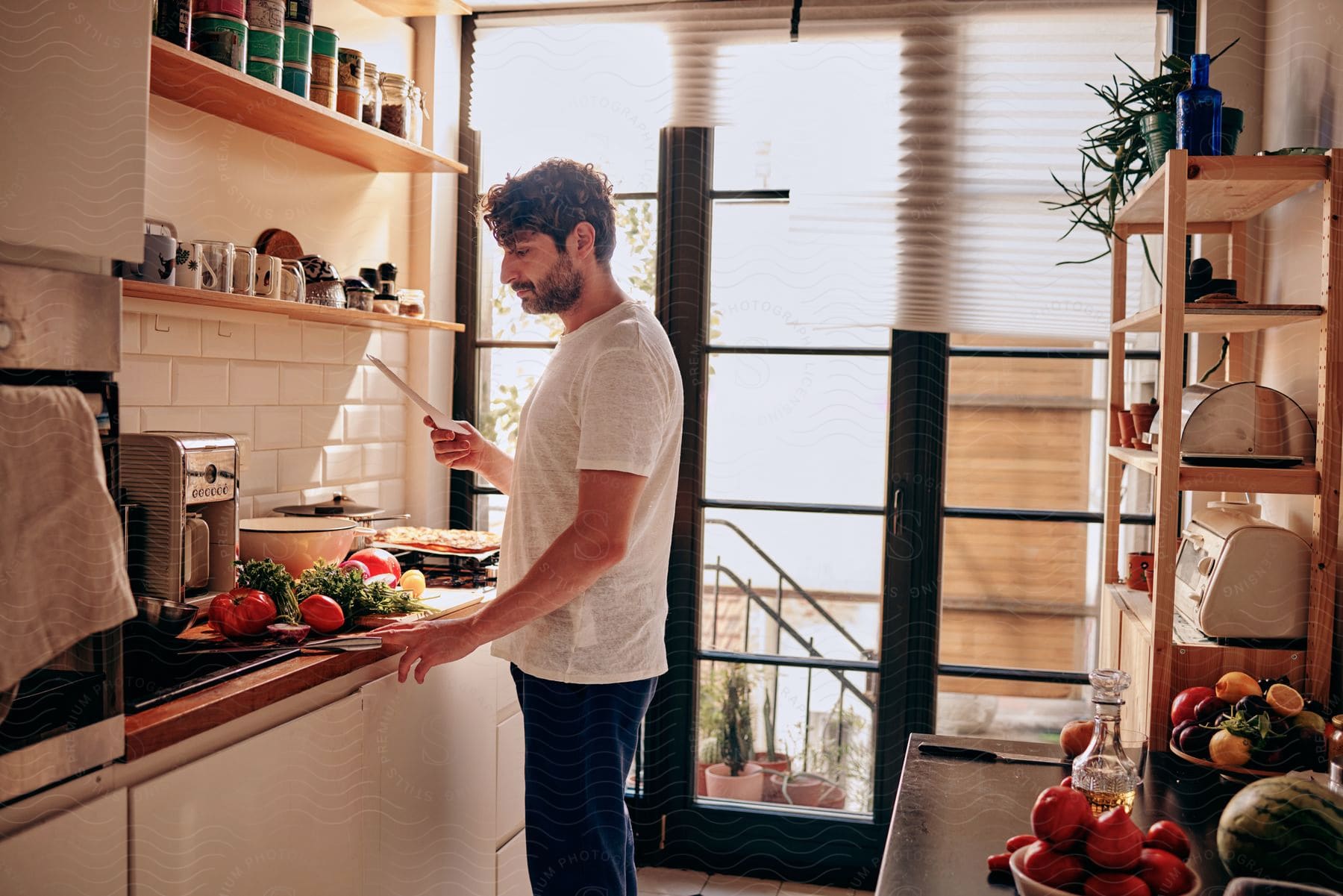 Man reading a recipe in the kitchen with the countertop filled with vegetables and greens.