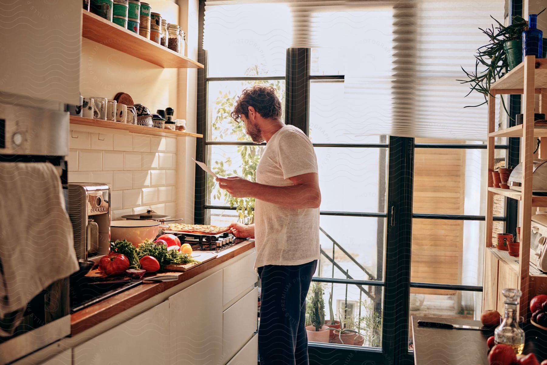 Stock photo of man in the kitchen holding a paper and observing a dough on the stove.