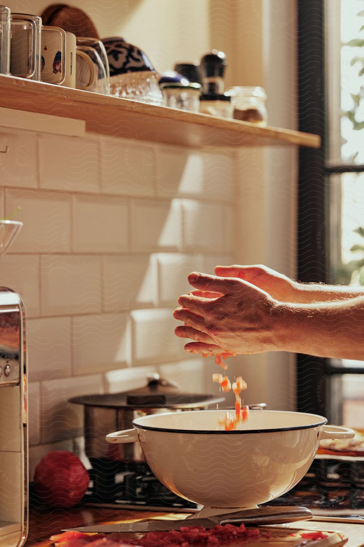 Man drops chopped tomatoes into a bowl while standing at the kitchen counter.