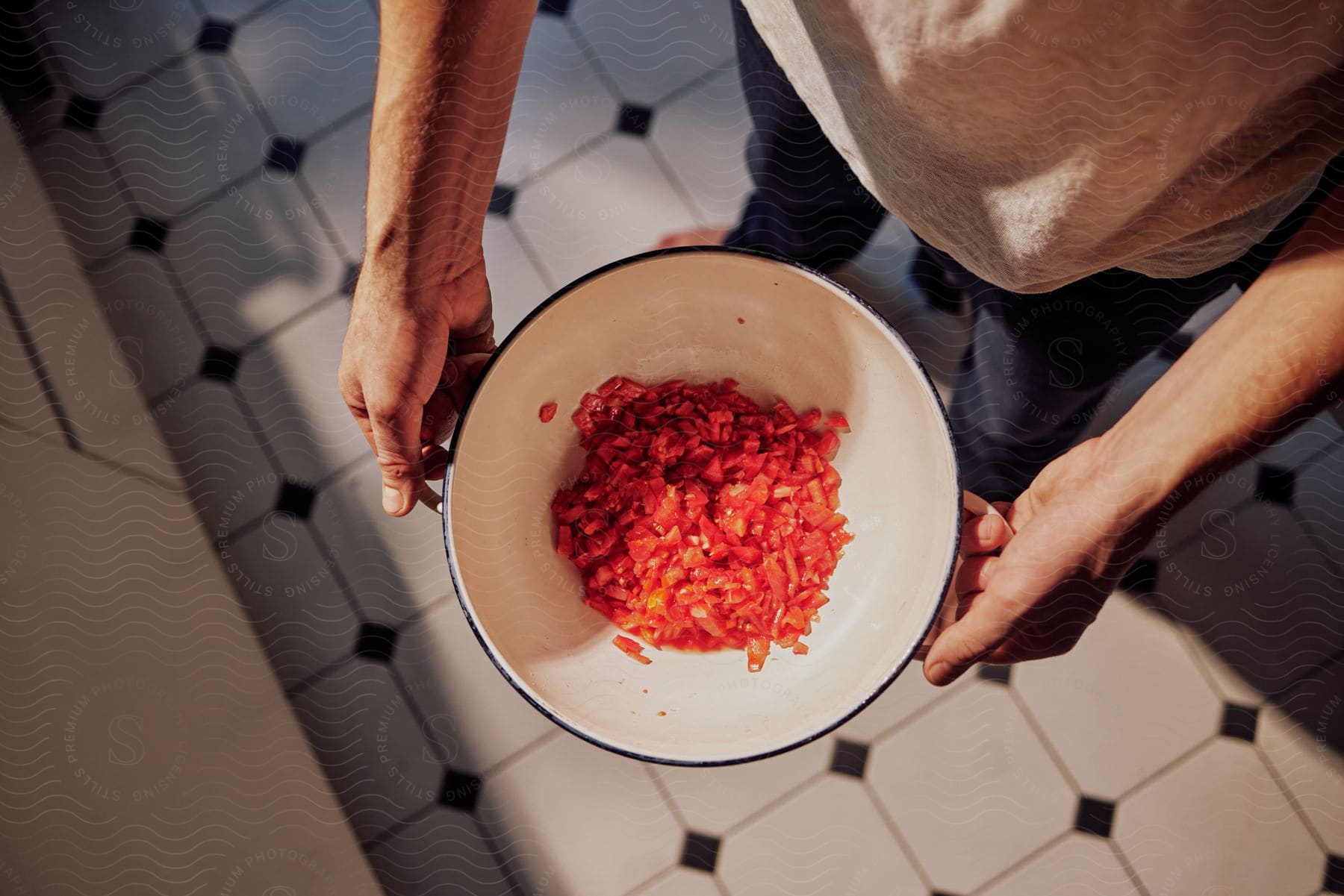 Man stands in kitchen holding bowl of chopped tomatoes.
