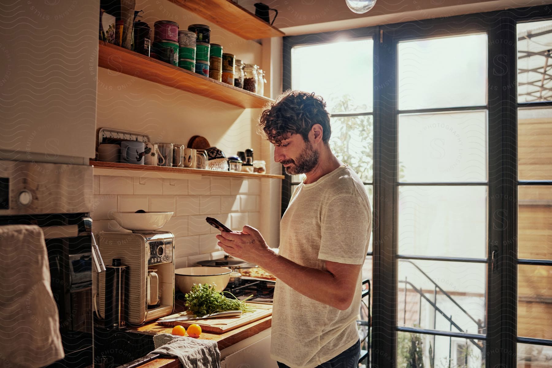 Man stands in kitchen near counter holding produce and checks his phone.