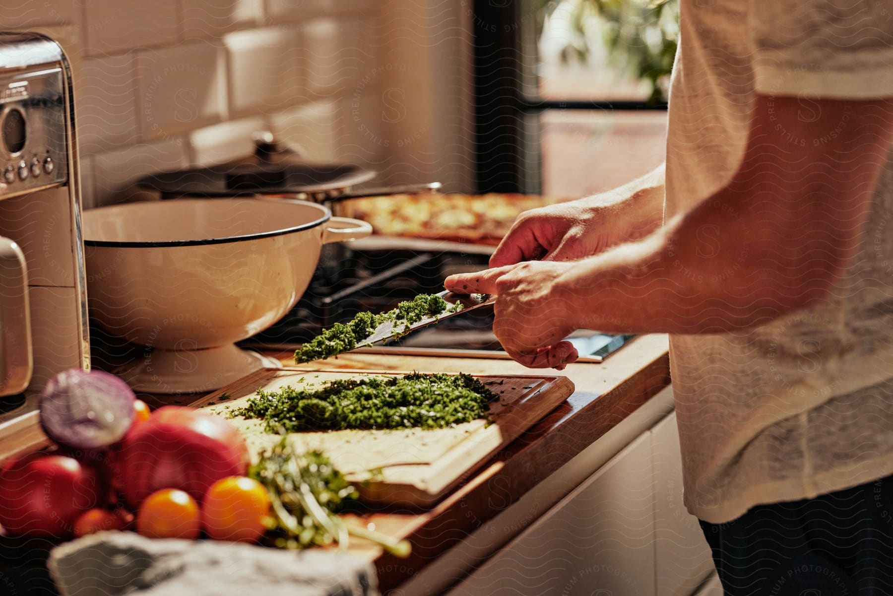 A man uses his finger to wipe the chopped parsley off his knife onto the wooden cutting board