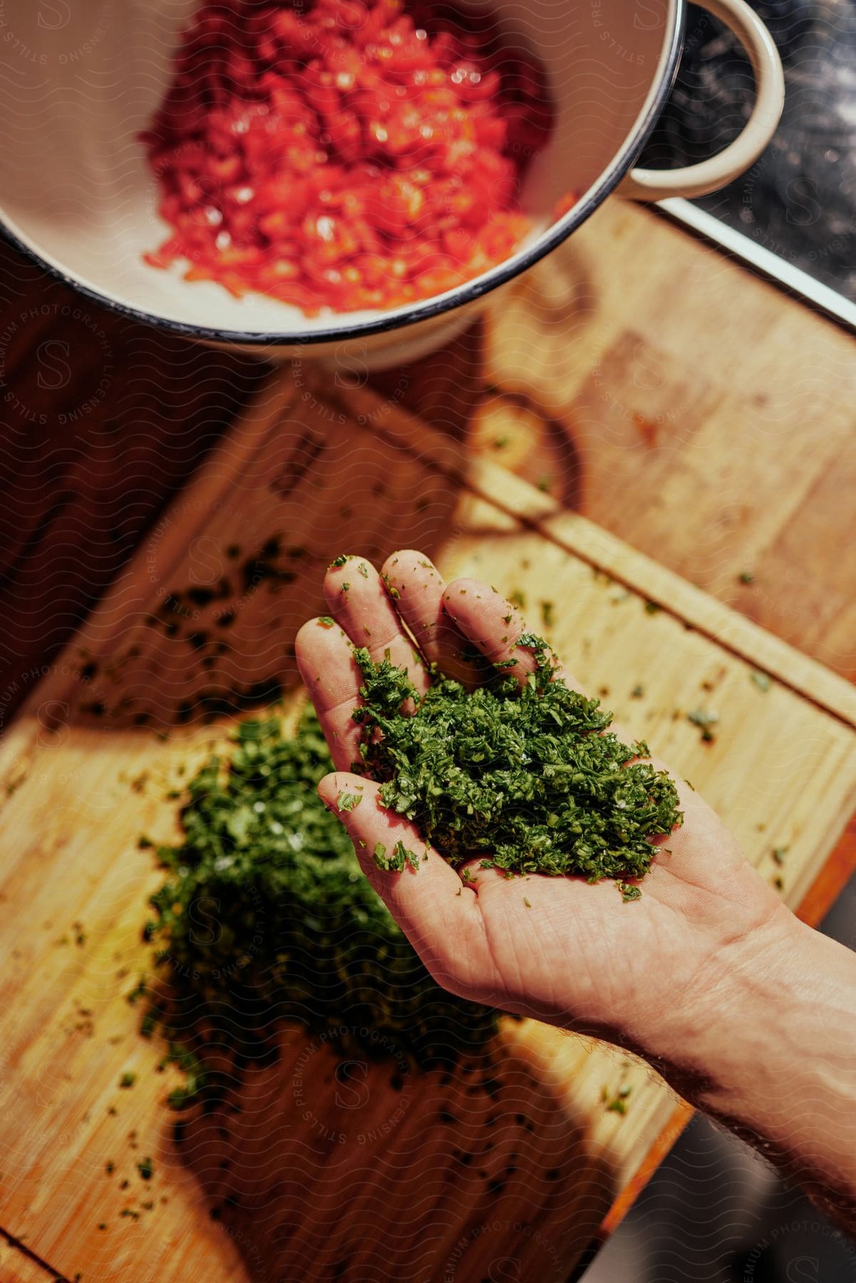 a hand holding a pile of chopped herbs over a cutting board.