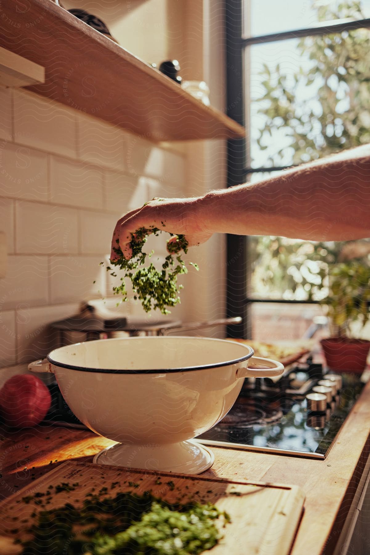 A cook is standing at the kitchen counter dropping chopped herbs into a bowl