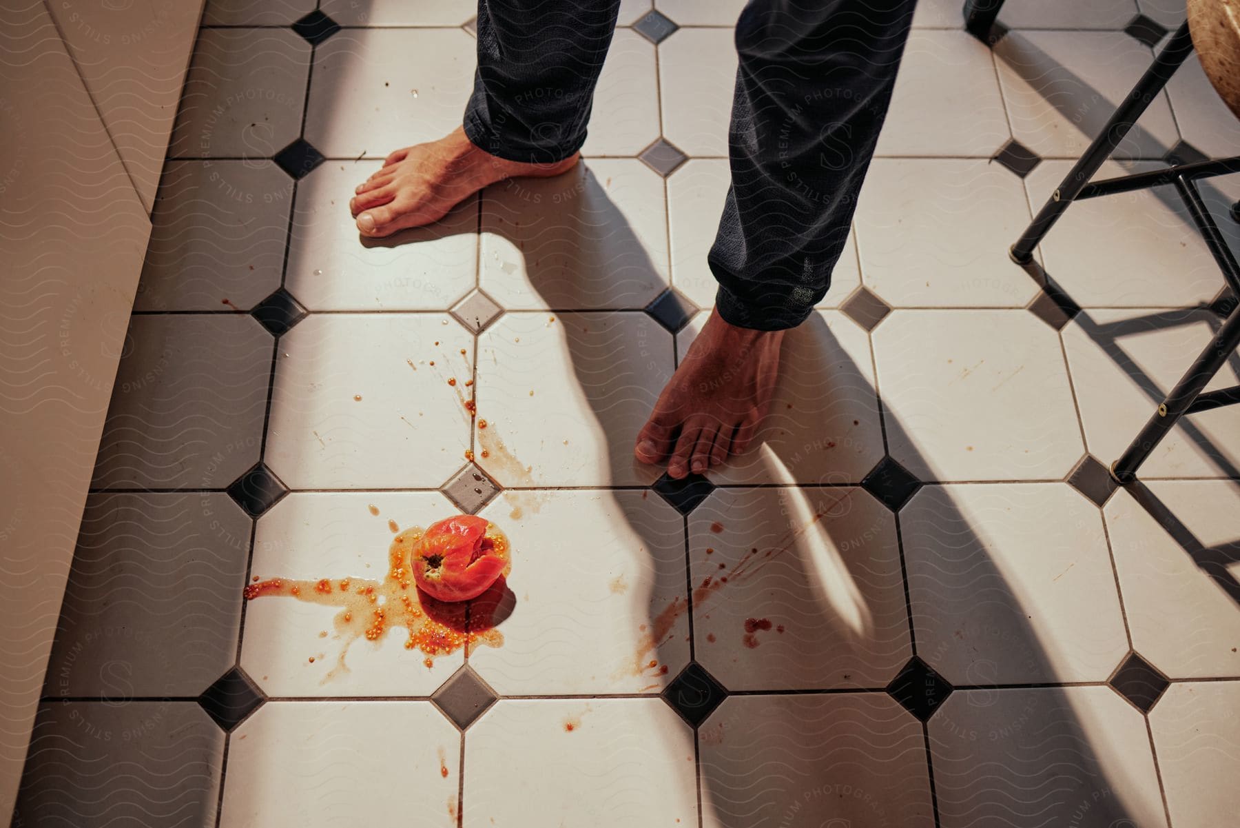 Man stands on kitchen tiles splattered by fallen tomato.