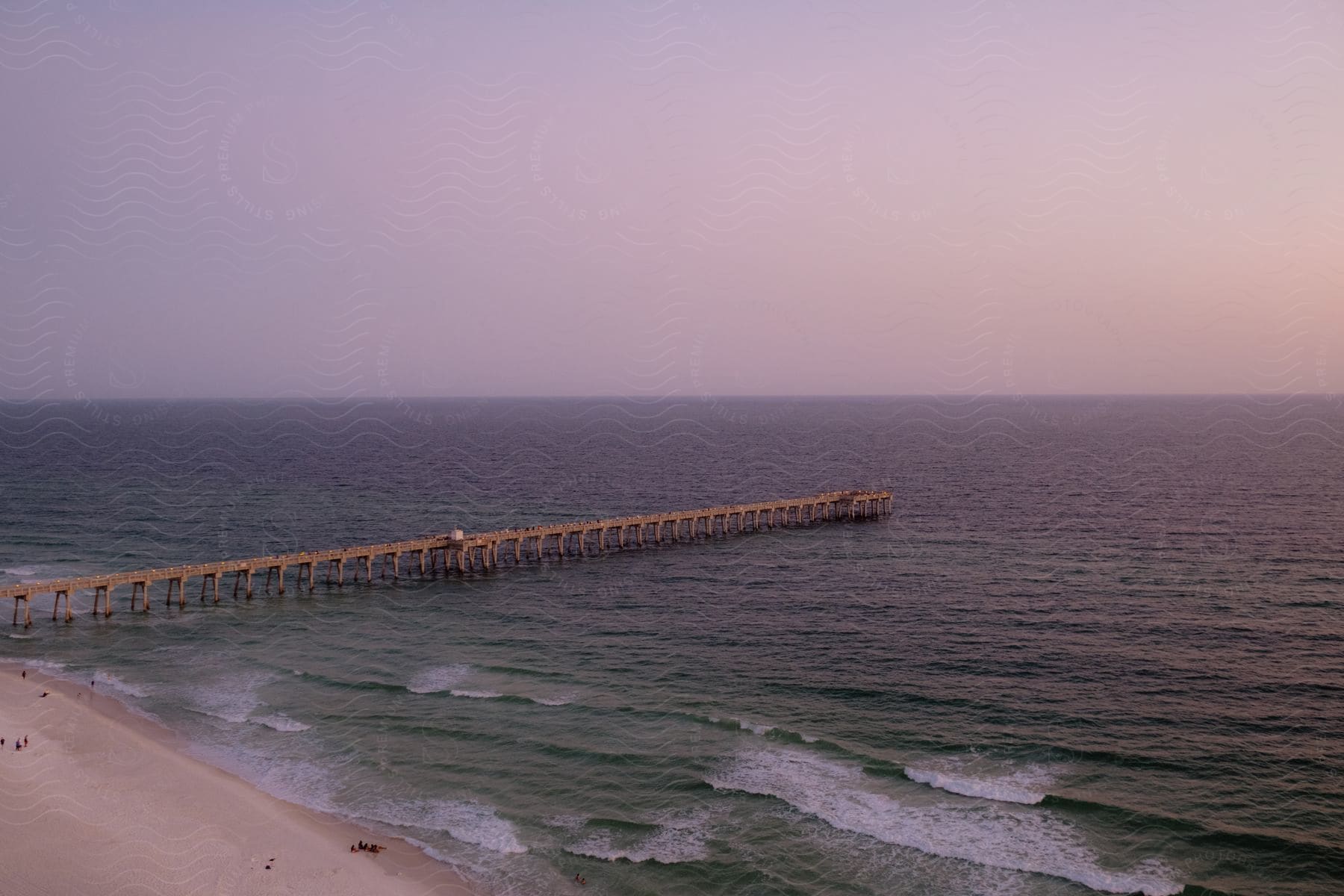 People are on the beach as waves roll into shore and a pier stretches out in the water