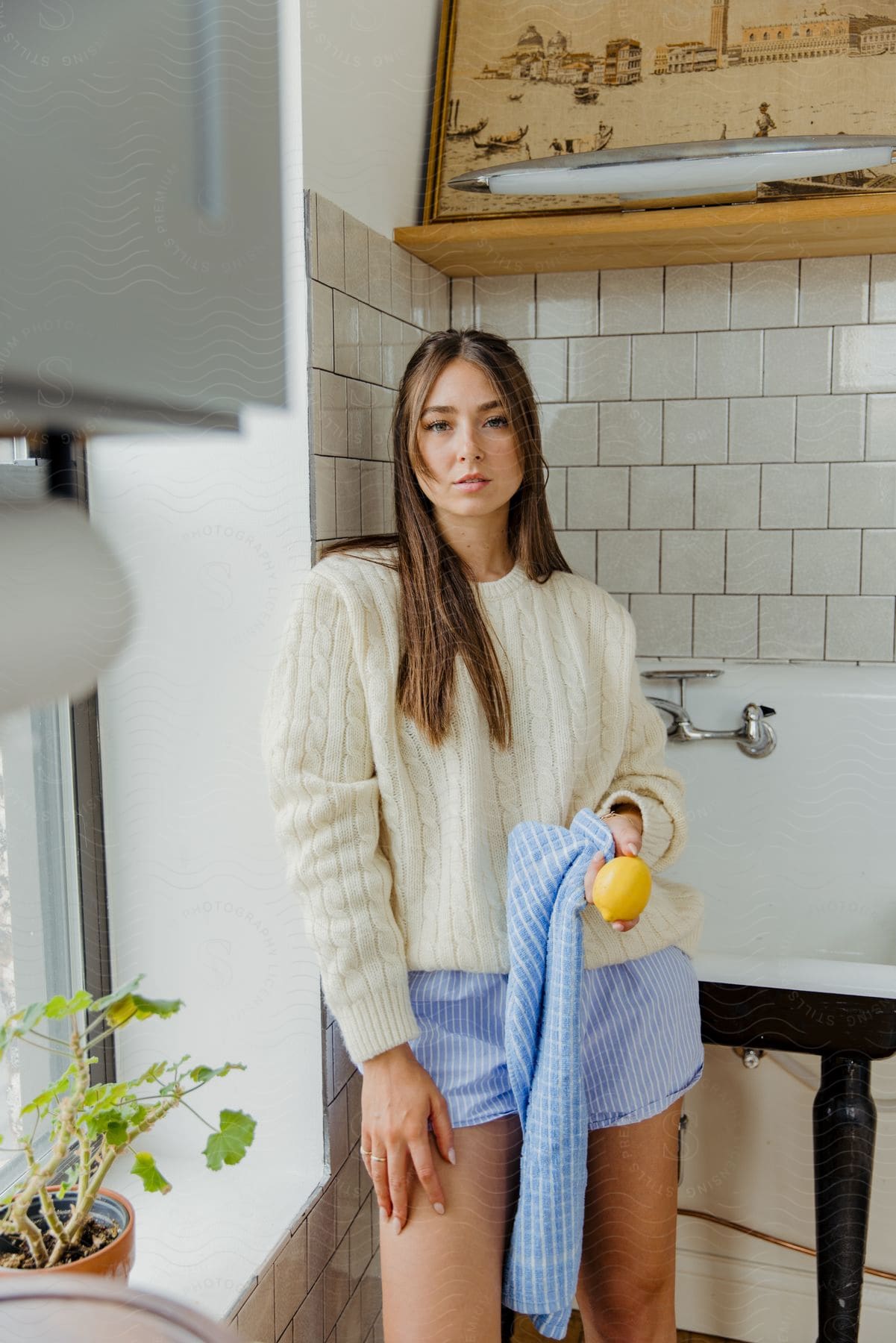 Woman posing indoors wearing a wool sweater, blue shorts, and holding a Sicilian lemon.