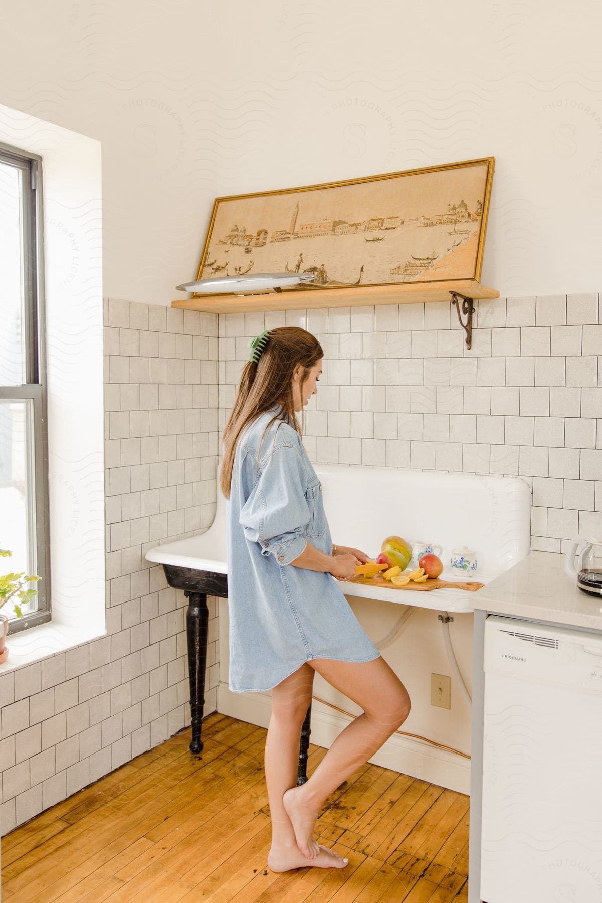 Stock photo of a woman cutting fruit in a kitchen during the middle of a day.