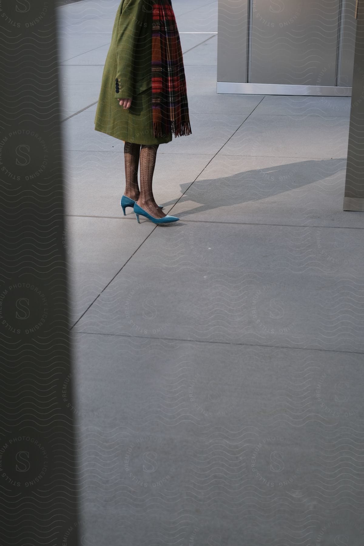 A woman modeling a long coat, scarf, and shoes outdoors.