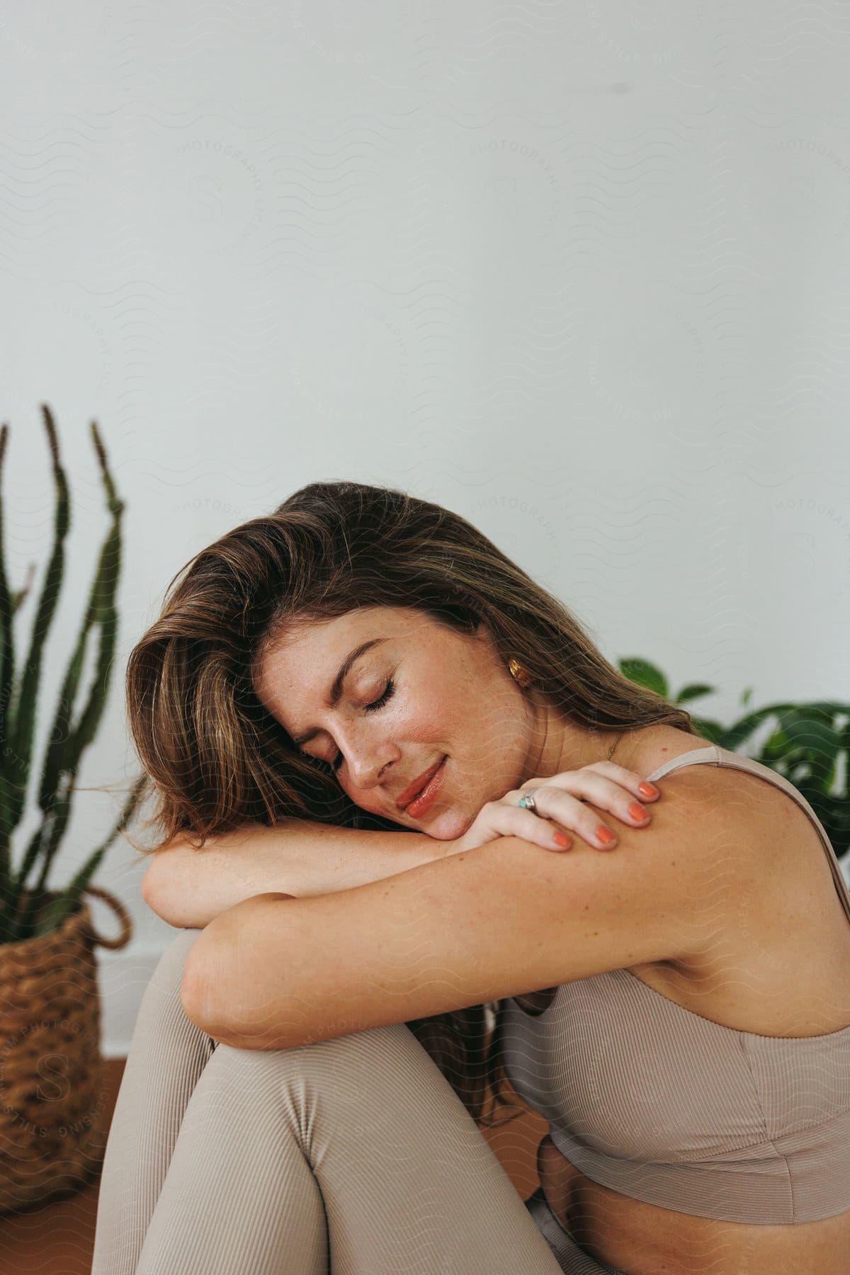 A woman, dressed in a sports bra and leggings, sits with her arms on her knees, wearing a smile of contentment.