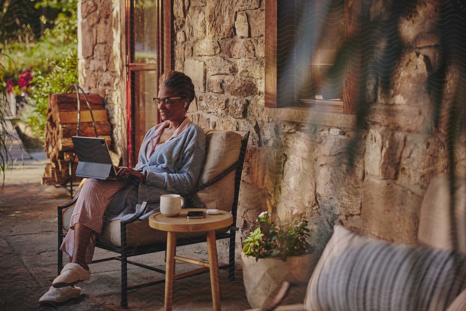 black woman sits on chair in front of stone house using ipad