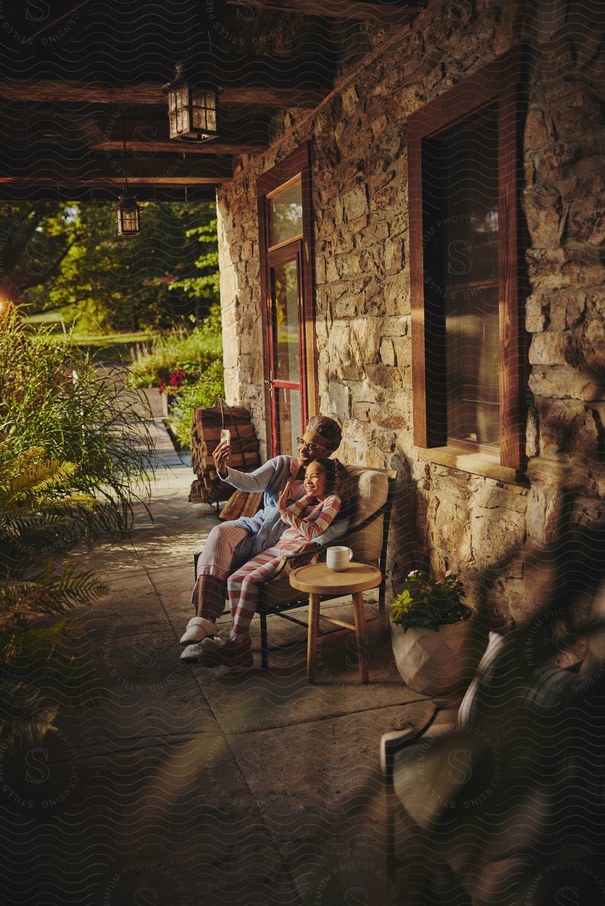 A grandmother and granddaughter smiling while sitting on a bench together at a house.